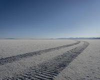 a pair of motorcycle tracks running through the desert plain on a sunny day with snow covered ground