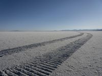 a pair of motorcycle tracks running through the desert plain on a sunny day with snow covered ground