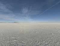 a lone person on a large ice covered field with some desert around it in the background