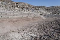 a dirt road in the middle of an empty desert, with hills in the background