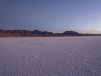 a snow covered landscape and several mountains on the far side of a flat desert plain