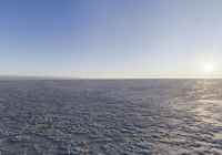 the view of a sun shining through the sky over a vast desert plain with footprints of people