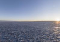 the view of a sun shining through the sky over a vast desert plain with footprints of people