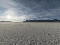 a single cloud is rising over a barren landscape in the middle of nowhere, with tracks and footprints, in this image