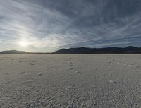 a single cloud is rising over a barren landscape in the middle of nowhere, with tracks and footprints, in this image