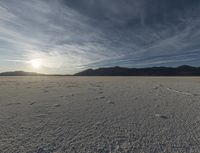 a single cloud is rising over a barren landscape in the middle of nowhere, with tracks and footprints, in this image