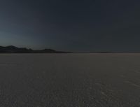 a picture that shows the dark sky above a vast plain of sand and hills at sunset