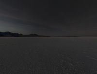 a picture that shows the dark sky above a vast plain of sand and hills at sunset