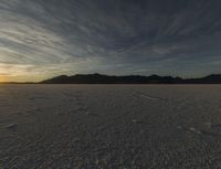 a desert with tracks and footprints of people on the sand at sunset and a mountain range