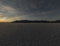 a desert with tracks and footprints of people on the sand at sunset and a mountain range