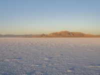 a person wearing red is walking in the desert with snow covering the ground and mountains behind him