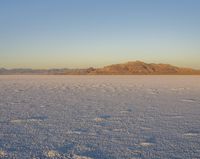 a person wearing red is walking in the desert with snow covering the ground and mountains behind him