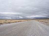 a deserted dirt road surrounded by clouds and power poles on both sides of it in the desert