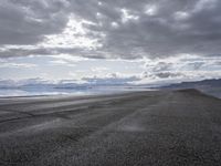 a dirt road stretches from the ocean, near a mountain range, on a cloudy day