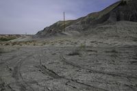 a dirt road in the middle of barren area with power lines overhead, and hills in background