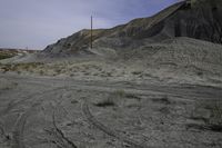 a dirt road in the middle of barren area with power lines overhead, and hills in background