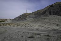 a dirt road in the middle of barren area with power lines overhead, and hills in background