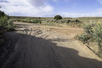 dirt road with gravel and brush near hills and cloudy blue sky with white clouds,