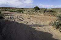 dirt road with gravel and brush near hills and cloudy blue sky with white clouds,