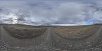 a panorama is shown of a dirt slope with clouds in the background and a blue sky with some snow