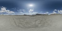 a wide open area with some large sand dunes in the background with a sky and clouds