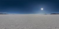 a wide shot looking down at a frozen plain under a bright sky with clouds, sun and mountains