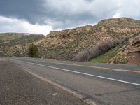 a man riding his motorcycle down the middle of a long road with some mountains in the background