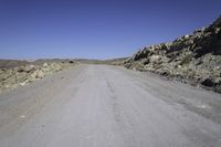 a lone motorcycle on the gravel road near some rocks and mountains in the background are shadows on the road