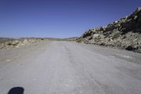 a lone motorcycle on the gravel road near some rocks and mountains in the background are shadows on the road