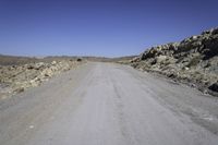 a lone motorcycle on the gravel road near some rocks and mountains in the background are shadows on the road