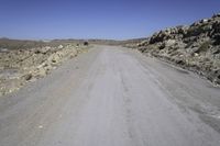 a lone motorcycle on the gravel road near some rocks and mountains in the background are shadows on the road