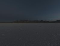 a field is empty with a lot of snow on it and mountains in the distance