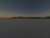 a field is empty with a lot of snow on it and mountains in the distance