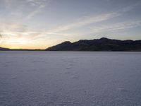 a lone person on a snow covered plain at sunset with mountains in the background with footprints