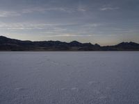 a lone person on a snow covered plain at sunset with mountains in the background with footprints