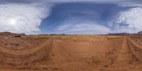 a dirt track with rocks and mountains in the distance and clouds in the sky and clouds overhead