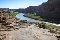 a person is standing on top of the rock ledge over looking the river in the distance