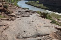 a person is standing on top of the rock ledge over looking the river in the distance