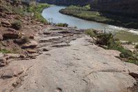 a person is standing on top of the rock ledge over looking the river in the distance