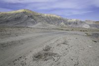 a dirt road in the middle of nowhere, with a rock formation on it near a large mountain