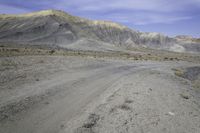 a dirt road in the middle of nowhere, with a rock formation on it near a large mountain