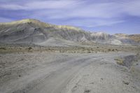 a dirt road in the middle of nowhere, with a rock formation on it near a large mountain