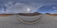 an empty street on a cloudy day with mountains behind it in the distance in a fish - eye lens