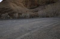 a person is skateboarding across the desert road towards a mountaintop with a small tree