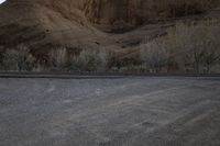 a person is skateboarding across the desert road towards a mountaintop with a small tree