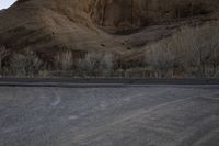 a person is skateboarding across the desert road towards a mountaintop with a small tree