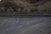 a person is skateboarding across the desert road towards a mountaintop with a small tree