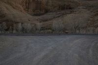 a person is skateboarding across the desert road towards a mountaintop with a small tree