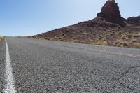 a person riding their bike down a deserted mountain road near a rock formation behind him