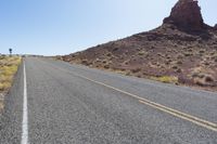 a person riding their bike down a deserted mountain road near a rock formation behind him